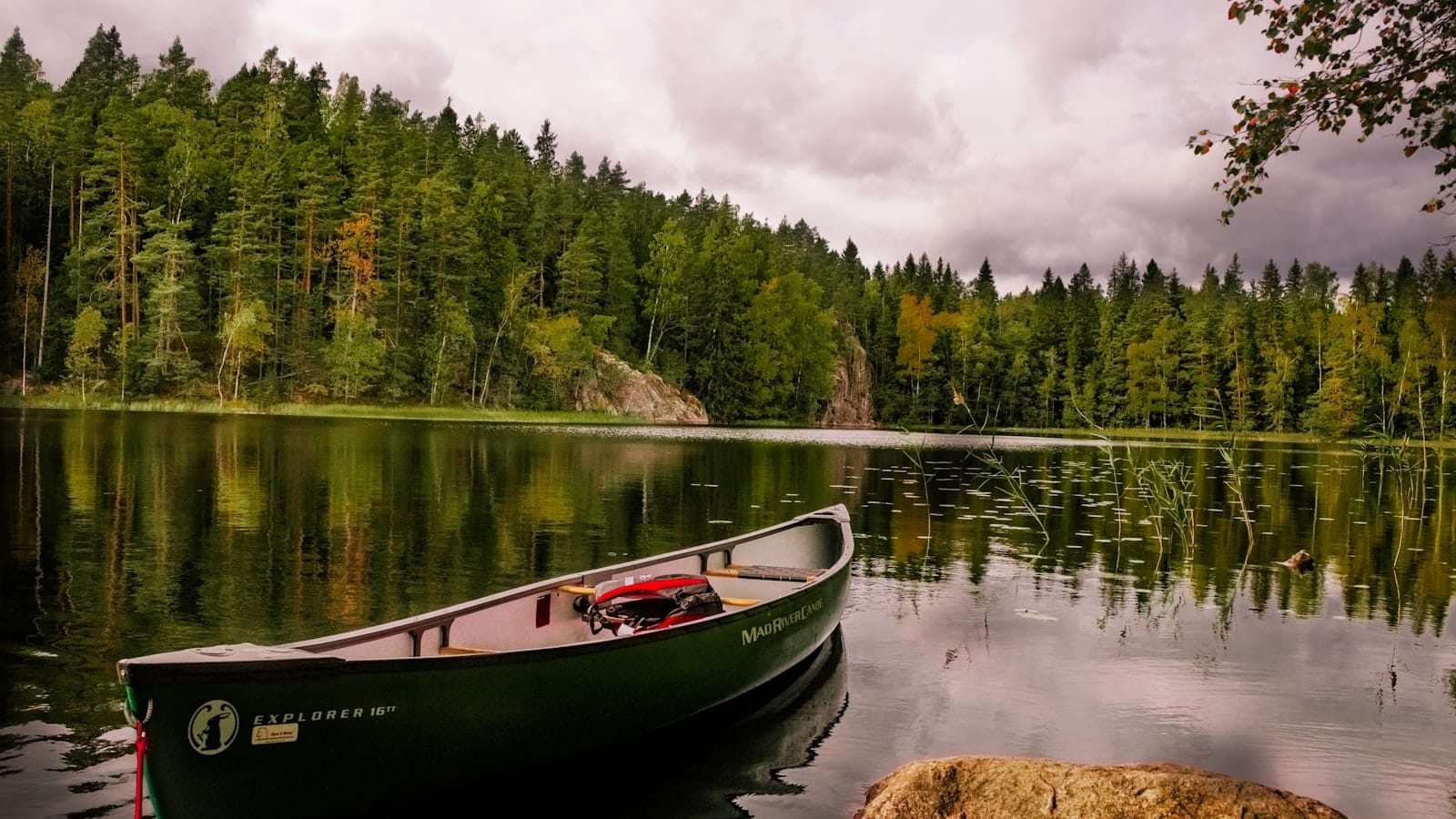 Canoë rouge et blanc posé sur un lac calme entouré de verdure