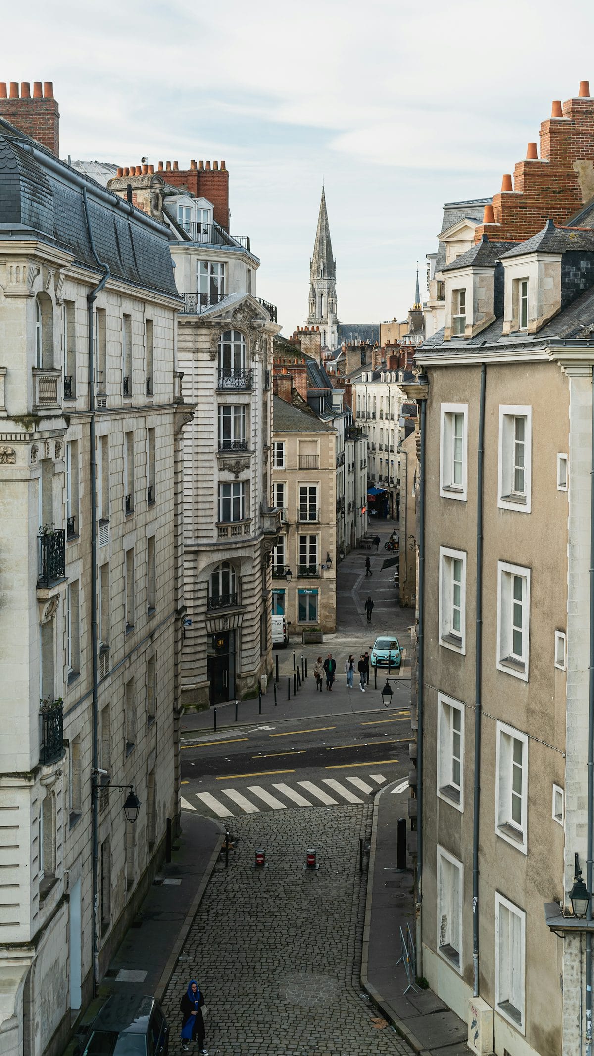 Rue animée du centre-ville de Nantes avec ses immeubles typiques et une tour d'horloge en arrière-plan