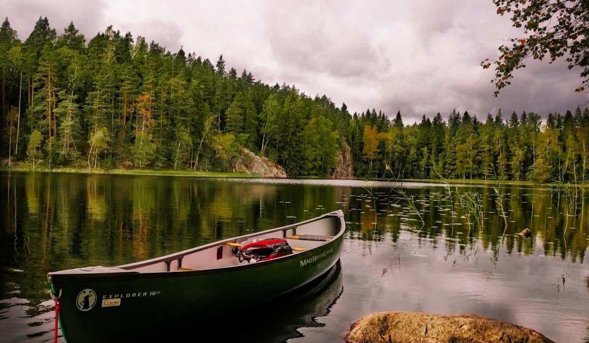 Canoë rouge et blanc posé sur un lac bordé d'arbres verts sous un ciel dégagé